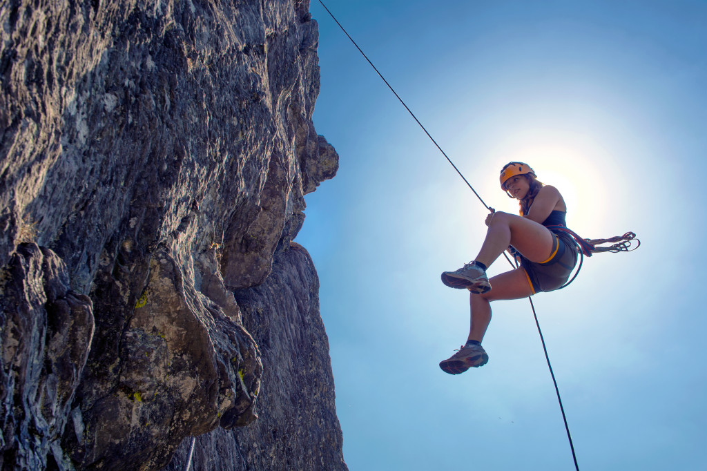 Young, tough, woman, abseiling from a steep rock, just in front of the sun