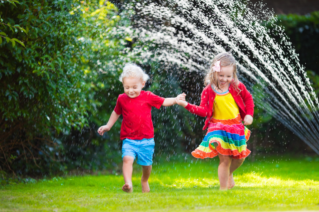 Little kids running on a green field with water splashing around