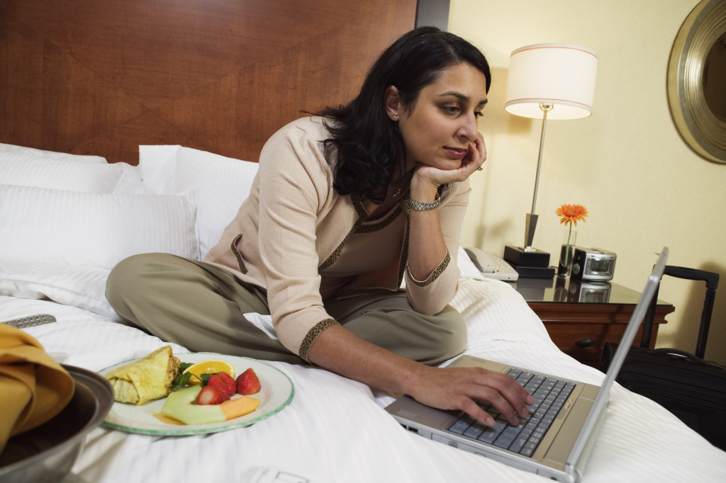 A woman working on her laptop in her hotel room while eating food