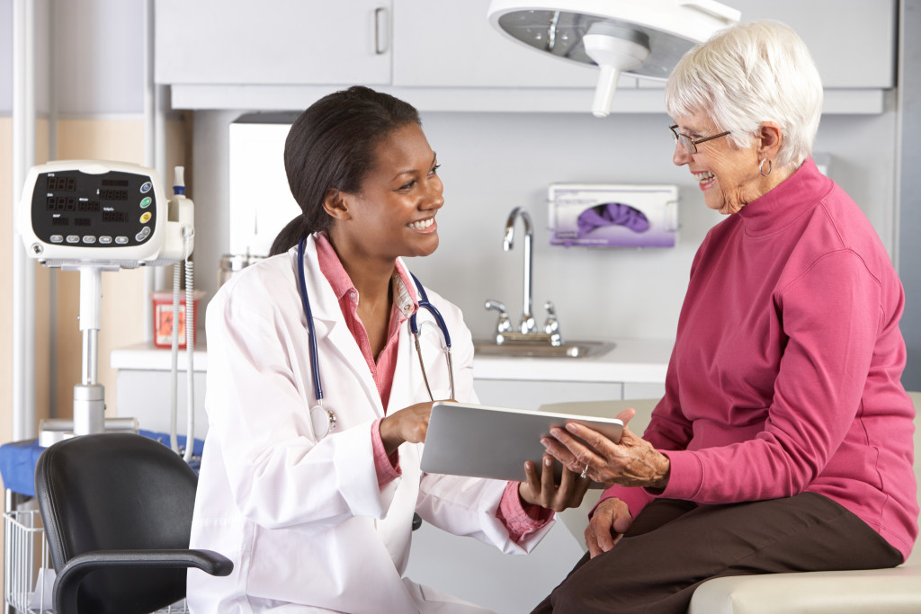 a female doctor talking to a senior patient showing a tablet device
